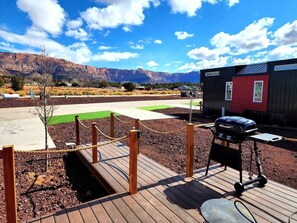 Une terrasse en bois avec un barbecue, un petit bâtiment rouge et, au loin, une vue sur la montagne.