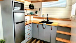 A compact kitchen with a built-in refrigerator, wooden countertops, grey cabinets, and a window above the sink. - Zion Couples’ Retreat • Romantic Desert Tiny Home (Apple Valley)