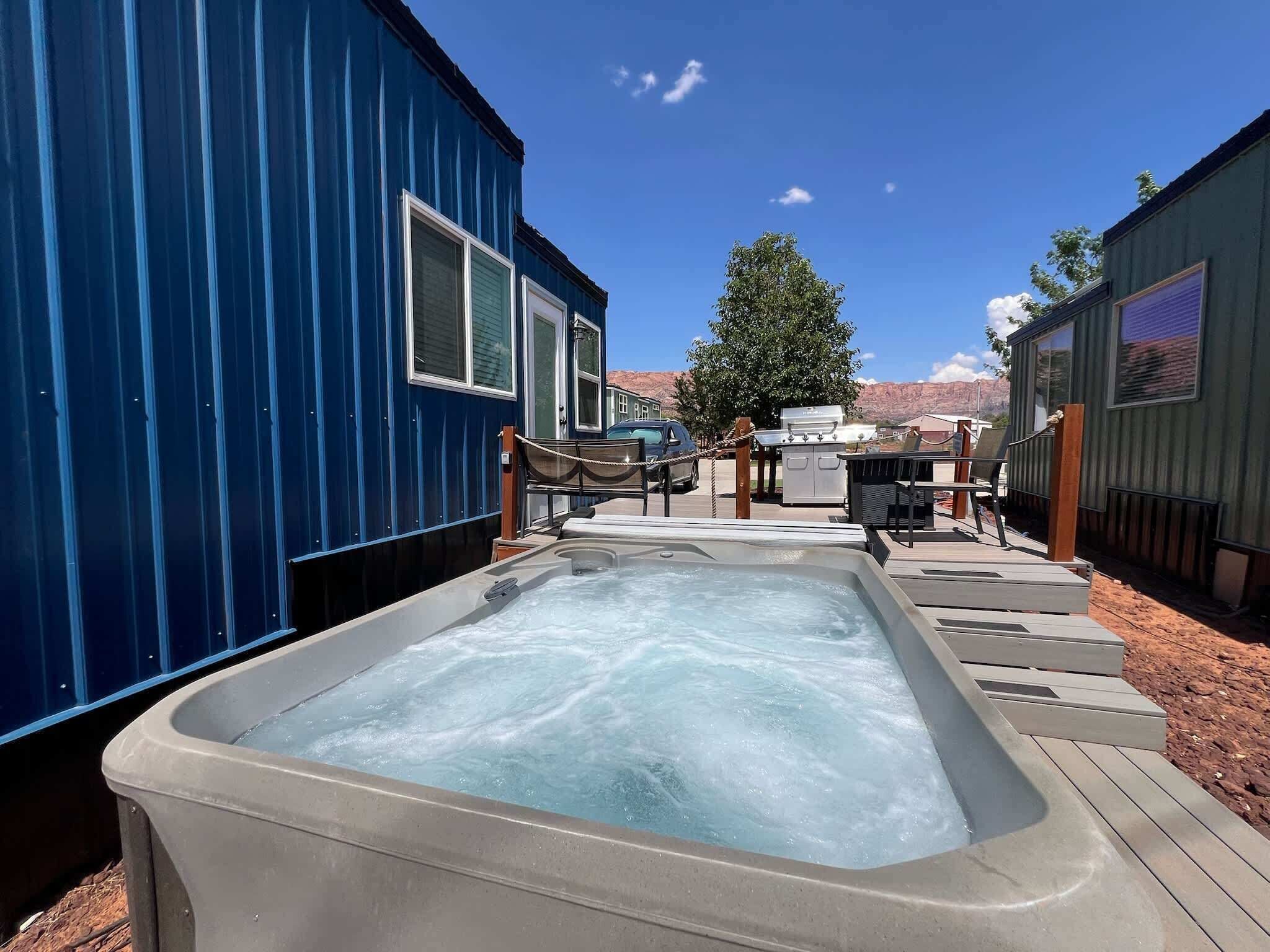 A hot tub area with a wooden deck, a barbecue grill, and a car parked nearby.