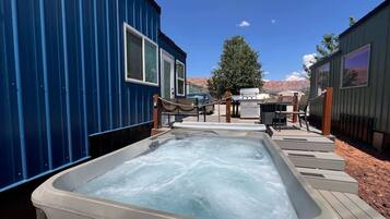 A hot tub area with a wooden deck, a barbecue grill, and a car parked nearby.