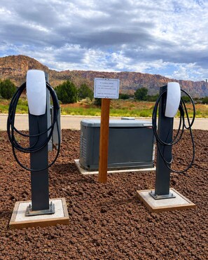 Two electric vehicle charging stations with a sign in the background, set against a rocky landscape with mountains. - Tiny Home + Private Hot Tub | Zion Adventure Base (Apple Valley)