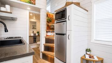 A modern kitchen with a stainless steel refrigerator, a built-in oven, and a microwave. There is a wooden countertop, a sink, and a window with blinds.
