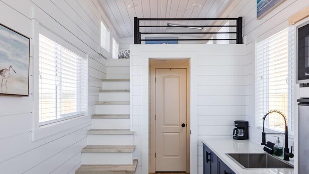 A modern kitchen with a wooden staircase, a black-framed window, and a kitchen island. - Zion Tiny Home Retreat w/ Hot Tub & Deck (Apple Valley)