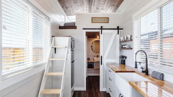 A compact, multi-functional space with a loft bed, built-in storage, a kitchen area, and a sliding door leading to a bathroom.