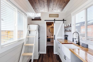 A compact, multi-functional space with a loft bed, built-in storage, a kitchen area, and a sliding door leading to a bathroom. - Family-Friendly Tiny Home • Firepit • BBQ • Zion (Apple Valley)
