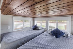 Ein Zimmer mit zwei Betten, Holzboden und großen Fenstern mit Jalousien.