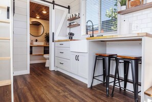 A modern kitchen with white cabinets, a wooden countertop, and two black bar stools. - Family-Friendly Tiny Home • Firepit • BBQ • Zion (Apple Valley)