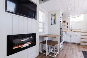 Una cocina moderna con armarios blancos, una chimenea empotrada, una mesa de madera y un cuadro en la pared.