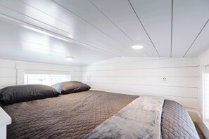 Une chambre à coucher avec un lit, deux oreillers, une fenêtre et un plafond doté d’un éclairage encastré.
