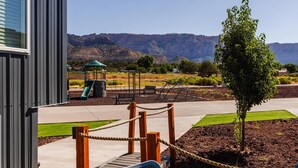Un parque infantil con tobogán, bancos y una zona vallada, con montañas al fondo.