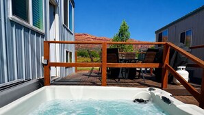 A hot tub with a wooden deck and chairs, a clear sky, and a mountain in the background. - Hot Tub Under Desert Sky • Zion Tiny Home Getaway (Apple Valley)