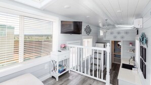 A bright, white interior with a skylight, a TV, and a staircase leading to a lower level. - Hot Tub Under Desert Sky • Zion Tiny Home Getaway (Apple Valley)