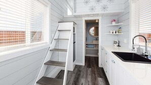 A compact kitchen with white cabinetry, a black sink, and a wooden staircase. - Hot Tub Under Desert Sky • Zion Tiny Home Getaway (Apple Valley)
