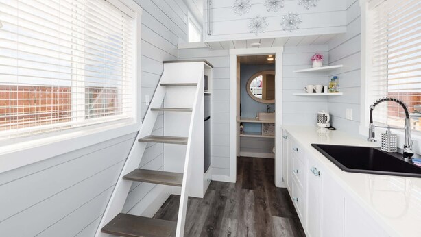 A compact kitchen with white cabinetry, a black sink, and a wooden staircase. - Hot Tub Under Desert Sky • Zion Tiny Home Getaway (Apple Valley)