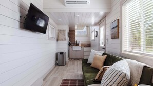 Et moderne interiør med et fladskærms-tv på væggen, et tekøkken og et hyggeligt opholdsområde med en grøn sofa.