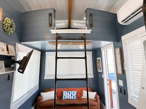A room with a blue wall, a brown leather sofa, a ladder, and a mounted TV. - Zion Stargazing Tiny Home • Deck + Red Rock Views (Apple Valley)
