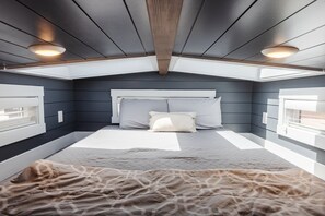 A bedroom with a sloped ceiling, skylight windows, a bed with a quilted cover, and a bedside table. - Zion Tiny Home Sleeps 4 • Deck + Red Rock Views (Apple Valley)