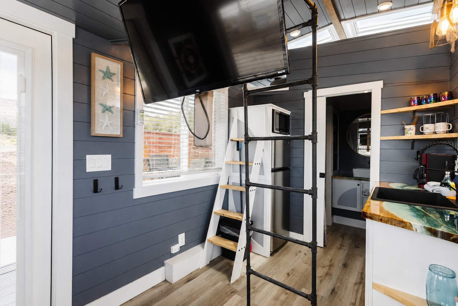 Een moderne keuken met een televisie bevestigd aan een zwarte metalen constructie, houten planken en een raam met jaloezieën.