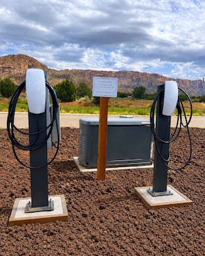 Twee elektrische oplaadpunten voor auto's, met een bord op de achtergrond, voor een rotsachtig landschap met bergen.