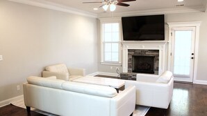 A living room with a white sofa, a coffee table, a fireplace, and a TV mounted above it. - 2027 Augusta Masters Week Luxury Rental, 7 Miles from Augusta National Golf Club (Martinez)