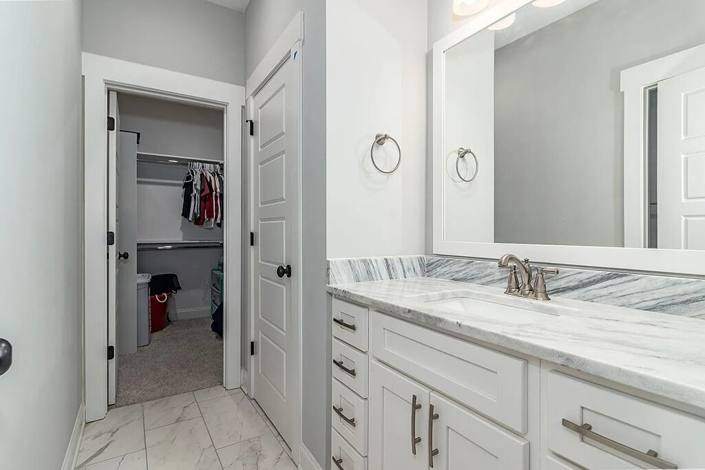 Une salle de bain moderne avec un comptoir en marbre, un grand miroir et un dressing où les vêtements sont suspendus.