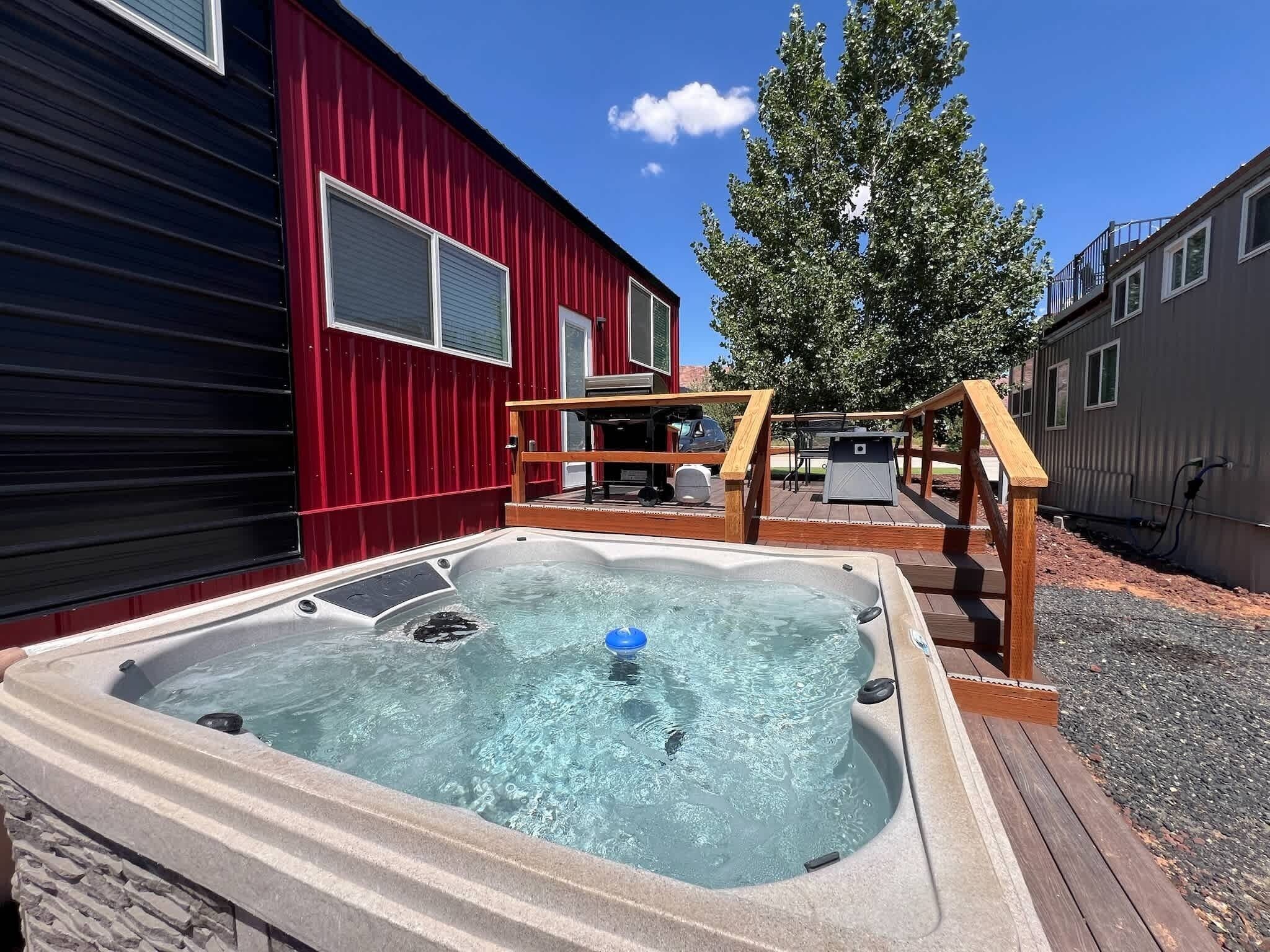 A hot tub in a backyard with a red building and a tree.