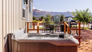 A hot tub with a wooden deck, a table with chairs, and a view of mountains in the background. - Zion Adventure • Private Hot Tub + Starry Nights (Apple Valley)
