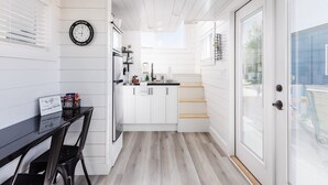 A modern kitchen with white cabinetry, a black clock, and a dining area with a black table and chairs. - Zion Basecamp • Tiny Home Near National Park (Apple Valley)