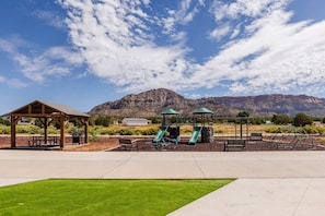 Ein Park mit einem Pavillon, Picknicktischen, einer Spielwiese mit Rutschen und einem Berg im Hintergrund.