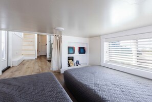 A modern bedroom with two beds, a window with blinds, a shelf with items, and a view of the outside. - Zion Adventure Tiny Home • Cozy Fireplace • Deck (Apple Valley)