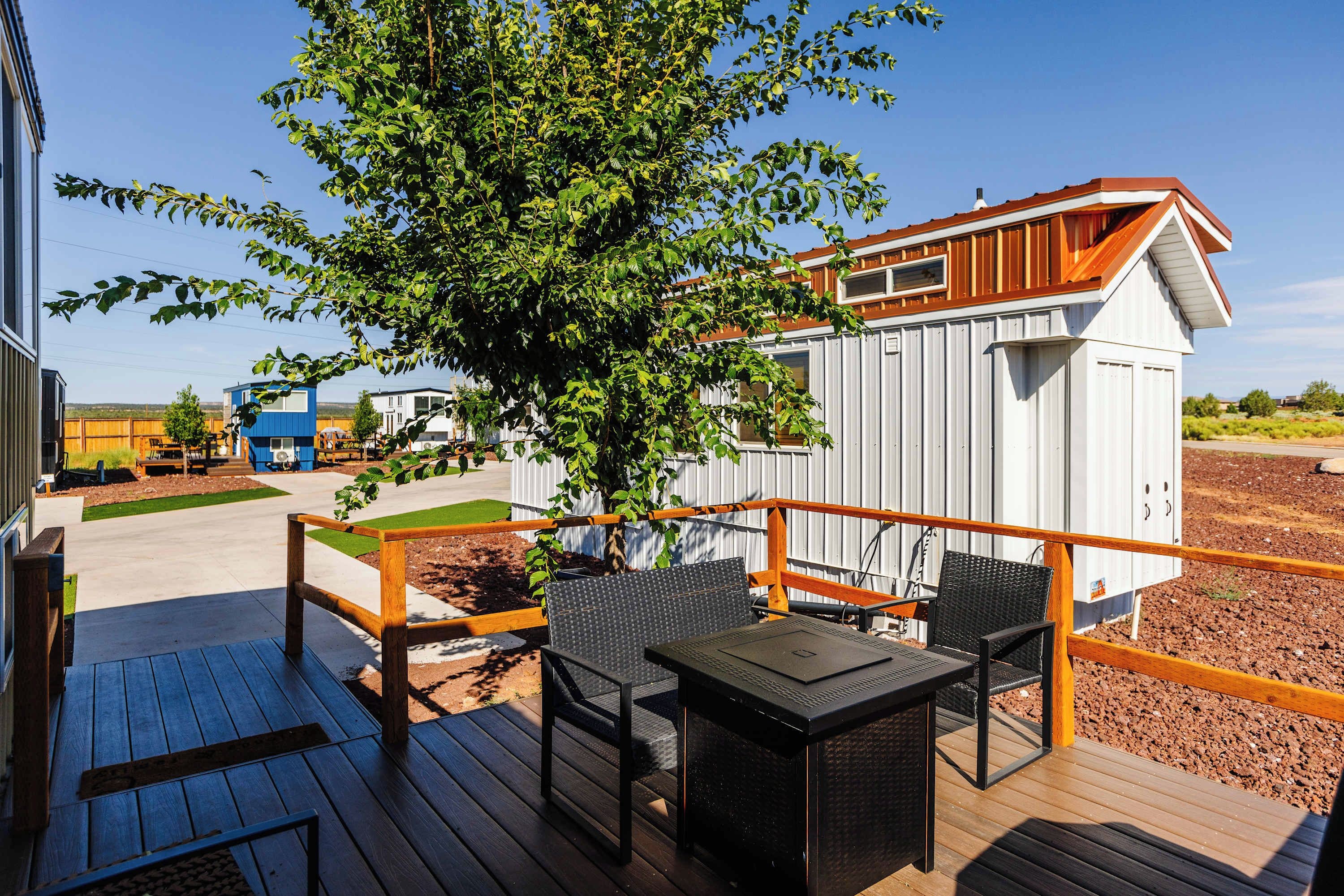 Una terraza con mobiliario exterior, un árbol y un edificio con fachada blanca y techo marrón.