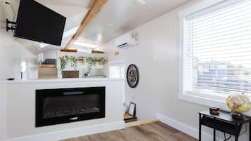 A modern living room with a fireplace, a mounted TV, and a large window with blinds.