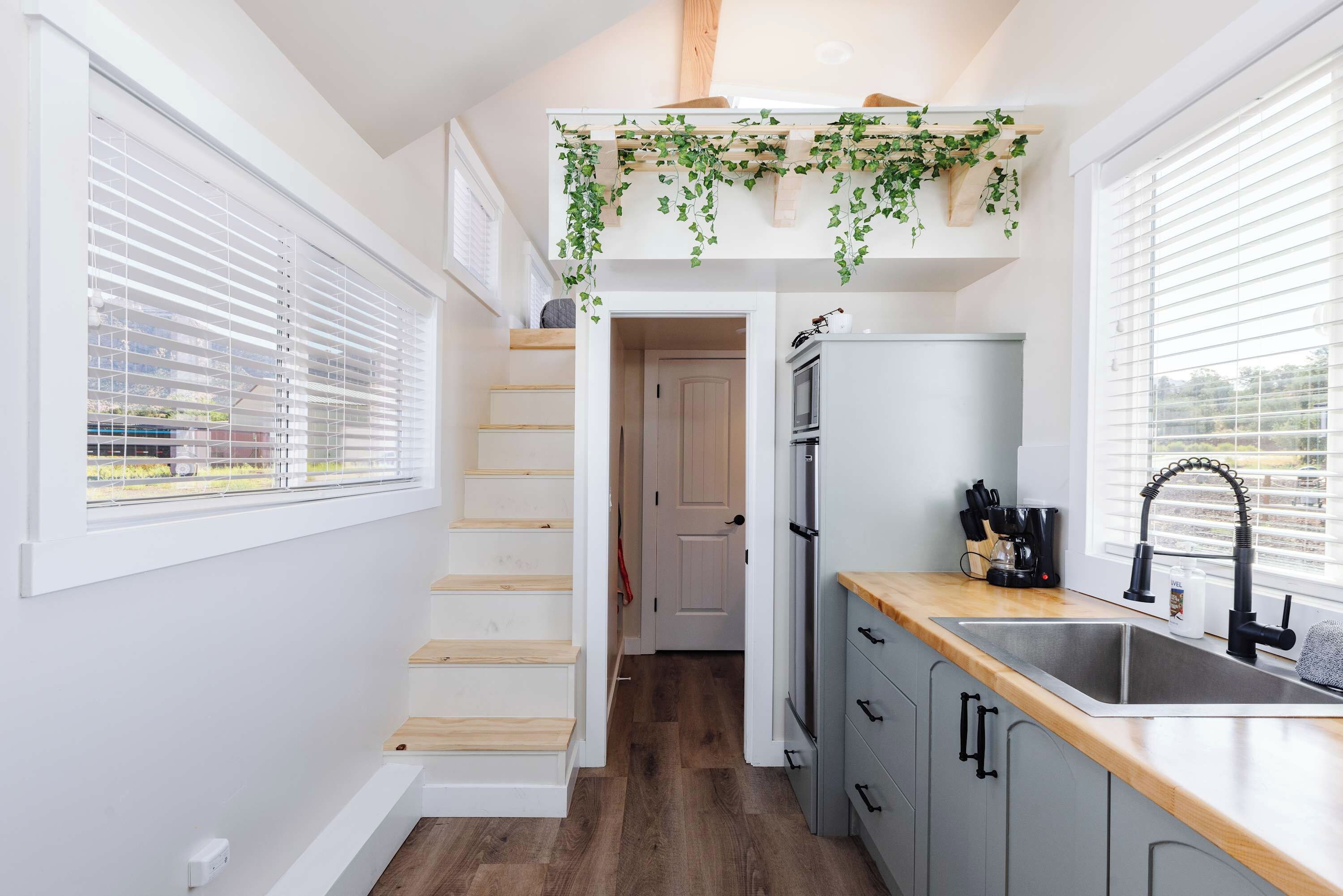 Une cuisine compacte avec un escalier en bois, un four encastré et une fenêtre équipée de stores.