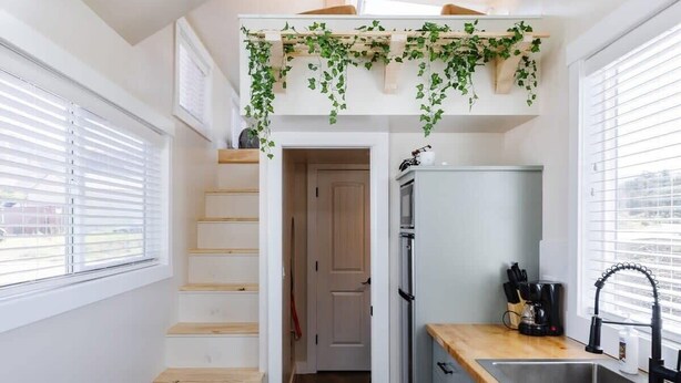 Une cuisine compacte avec un escalier en bois, un réfrigérateur encastré et une fenêtre équipée de stores.