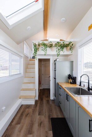 Eine kleine Küche mit einer Holztreppe, einem eingebauten Kühlschrank und einem Fenster mit Jalousien.