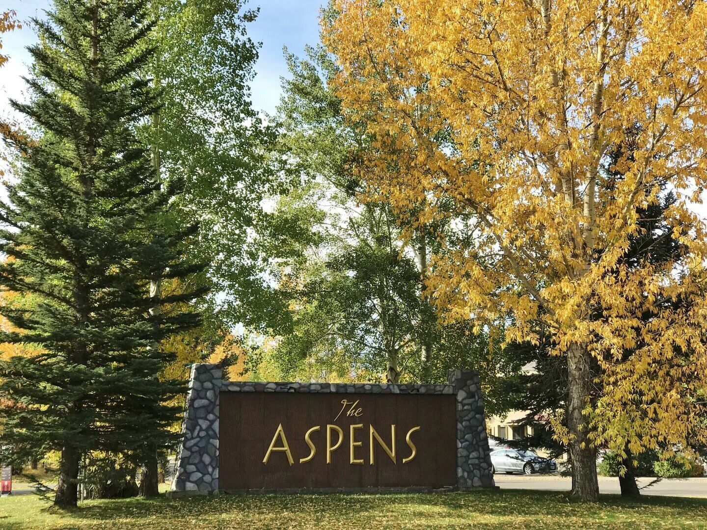 Segnaletica per 'The Aspens', con un muro in pietra e uno sfondo di alberi con foglie autunnali.
