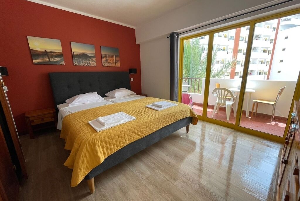 A hotel room with a bed, a balcony with a table and chairs, and a view of the city.