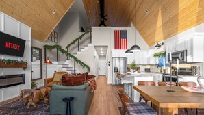 A modern kitchen with white cabinets, a wooden dining table, and a large TV displaying 'NETFLIX'. - Liezl Lane (Indian Point)