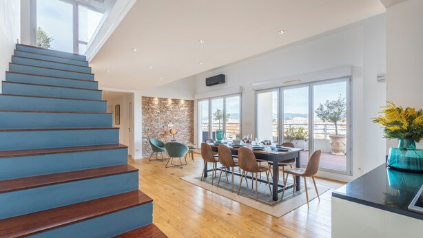 Un interno moderno con una scala in legno, un'area pranzo con sedie e un tavolo, e ampie finestre che offrono una vista.