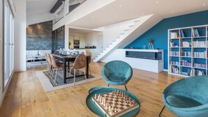 Un'ampia zona giorno con pavimento in legno, un tavolo da pranzo con sedie, una grande libreria e una scala che conduce a un piano superiore.