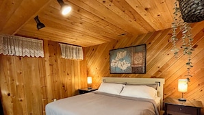 Un dormitorio acogedor con techo de madera, una cama grande, dos mesitas de noche con lámparas y una planta colgante.