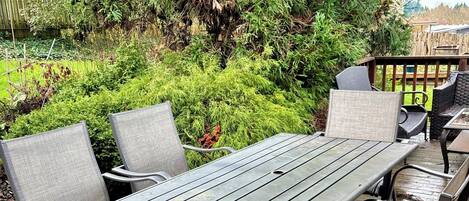 A wooden deck with a table and chairs, surrounded by lush greenery and a wooden fence.