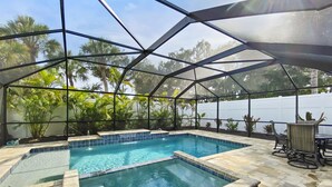 A covered outdoor swimming pool with a clear view of palm trees and a white fence in the background. - Modern Luxury Private Home with Pool in Siesta Key (Siesta Key)