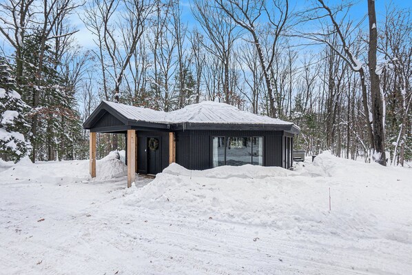 Una cabaña con fachada oscura, vigas de madera y techo cubierto de nieve.