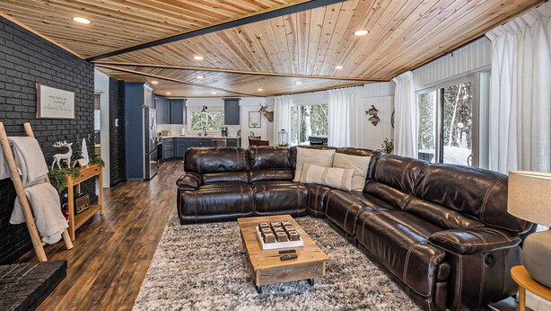 Un salón amplio con un sofá seccional de cuero grande, una mesa de centro de madera y una pared decorativa de ladrillo negro.