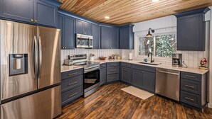 Una cocina moderna con armarios azul oscuro, electrodomésticos de acero inoxidable y techo de madera.