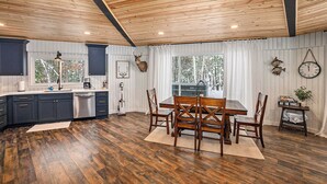 Una cocina con suelo de madera, una mesa de comedor con sillas, un lavamanos, armarios y un reloj en la pared.