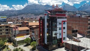 Un hôtel moderne à la façade rouge et blanche très visible, situé dans une région montagneuse et offrant une vue sur la ville et les montagnes en arrière-plan.