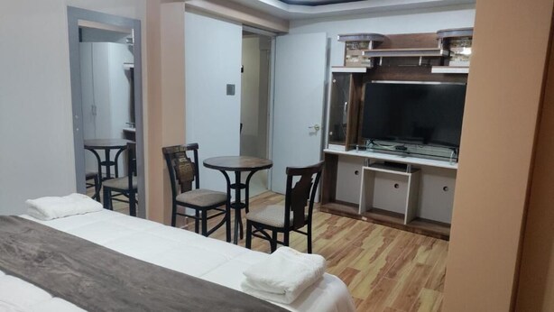 Une chambre d’hôtel comprenant un lit, une petite table à manger, deux chaises, un coin cuisine et un téléviseur.