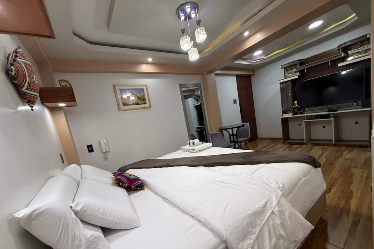 A hotel room with a large bed, a TV, a desk, and a chair.